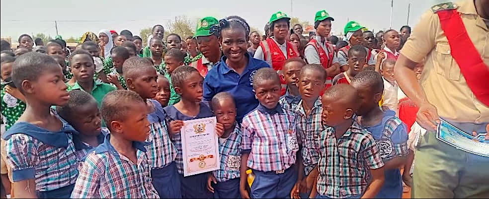 Learners crowding around a teacher holding up a certificate at an outdoor event