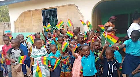 Young learners waving small Ghana flags in front of the school
